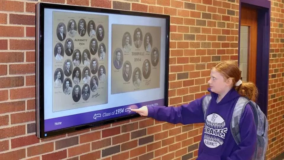 A student interacts with a lobby touchscreen showing a school's history of class photos.