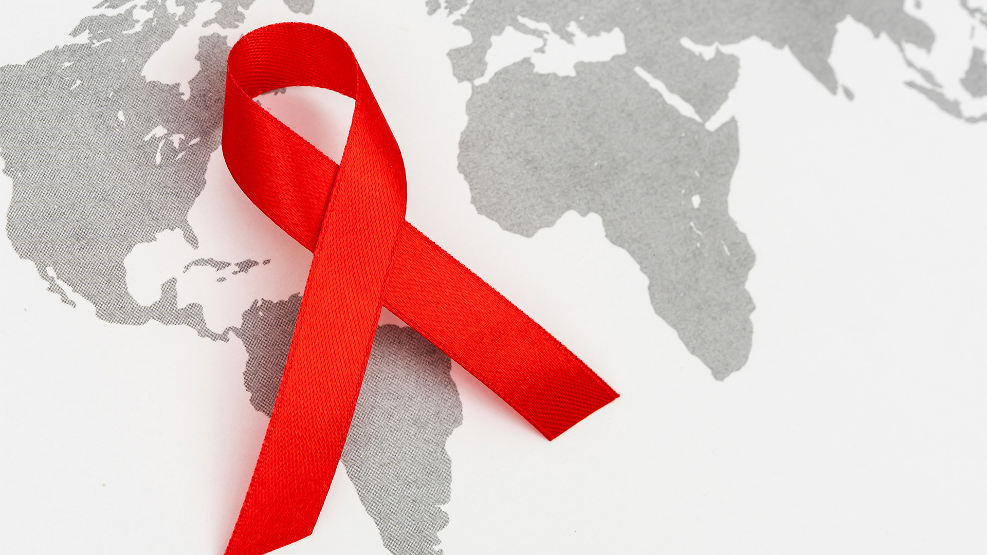 World Aids Day graphic of the word printed on fabric and a red ribbon place over the top of the world.