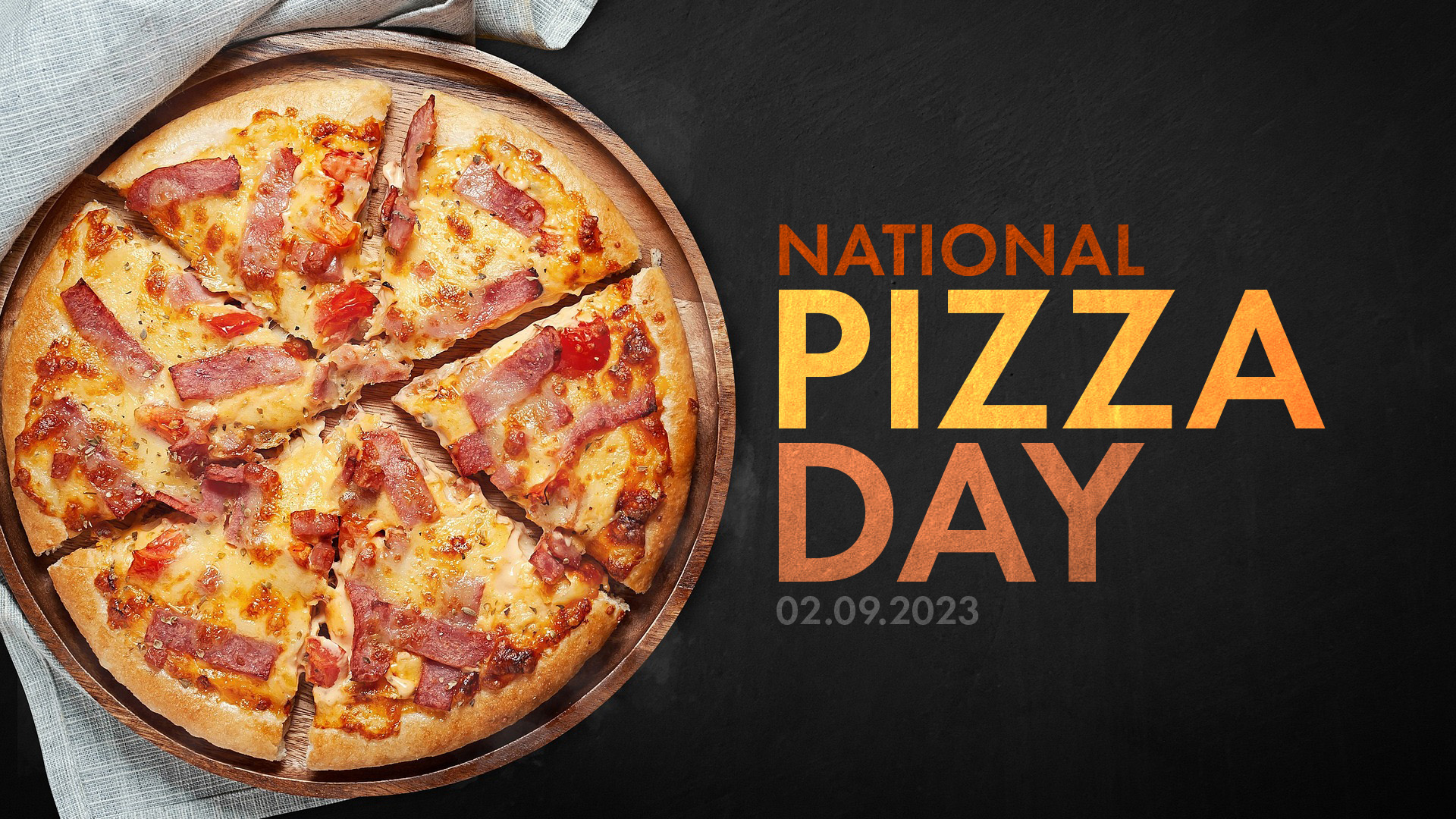 Ham, cheese, and tomato pizza on a wood round with a black textured background. 'National Pizza Day' written in a bold sans serif font.