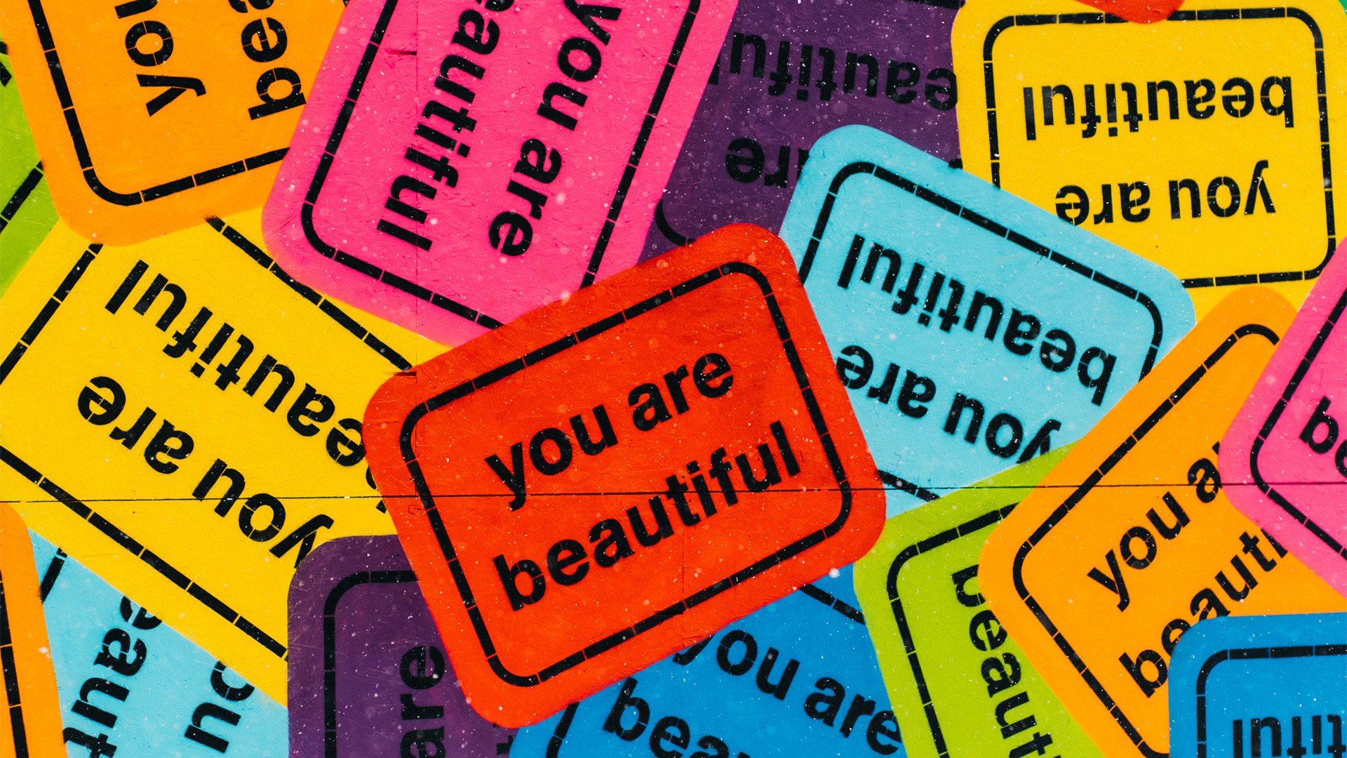 A very colorful graphic that appears to be different colored overlapping stickers that all say you are beautiful.