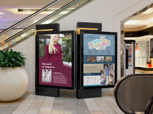 Digital Advertising display in a mall next to an elevator of a woman in a red dress on the left and a wayfinding display to the right 