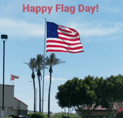 Animated graphic of a USA flag waving in the wind! There is a blue sky with little cloud coverage. Along the top center of the graphic red text reads Happy Flag Day!