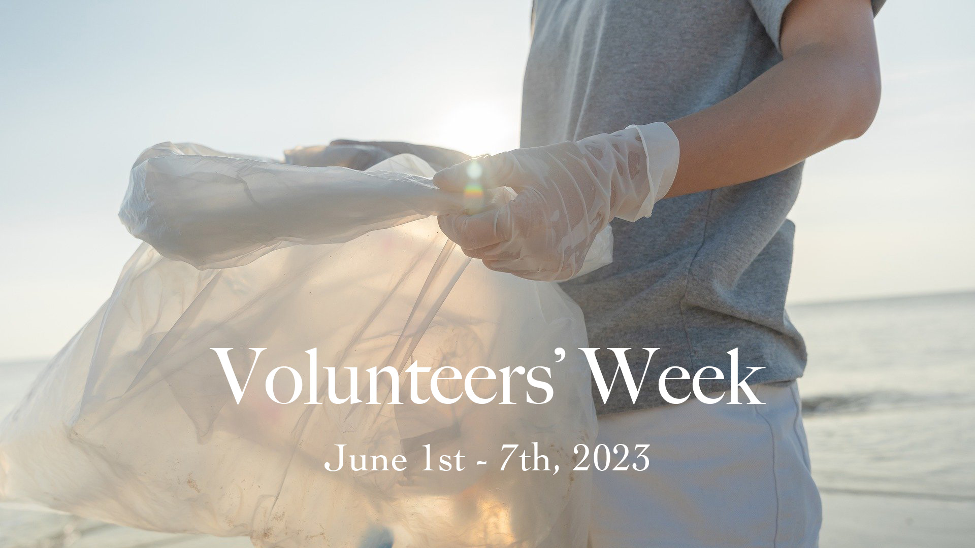 Younger child wearing gloves and holding a clear sack collecting garbage on the beach. Volunteers' Week June 1st - 7th, 2023 is written in white serif font.