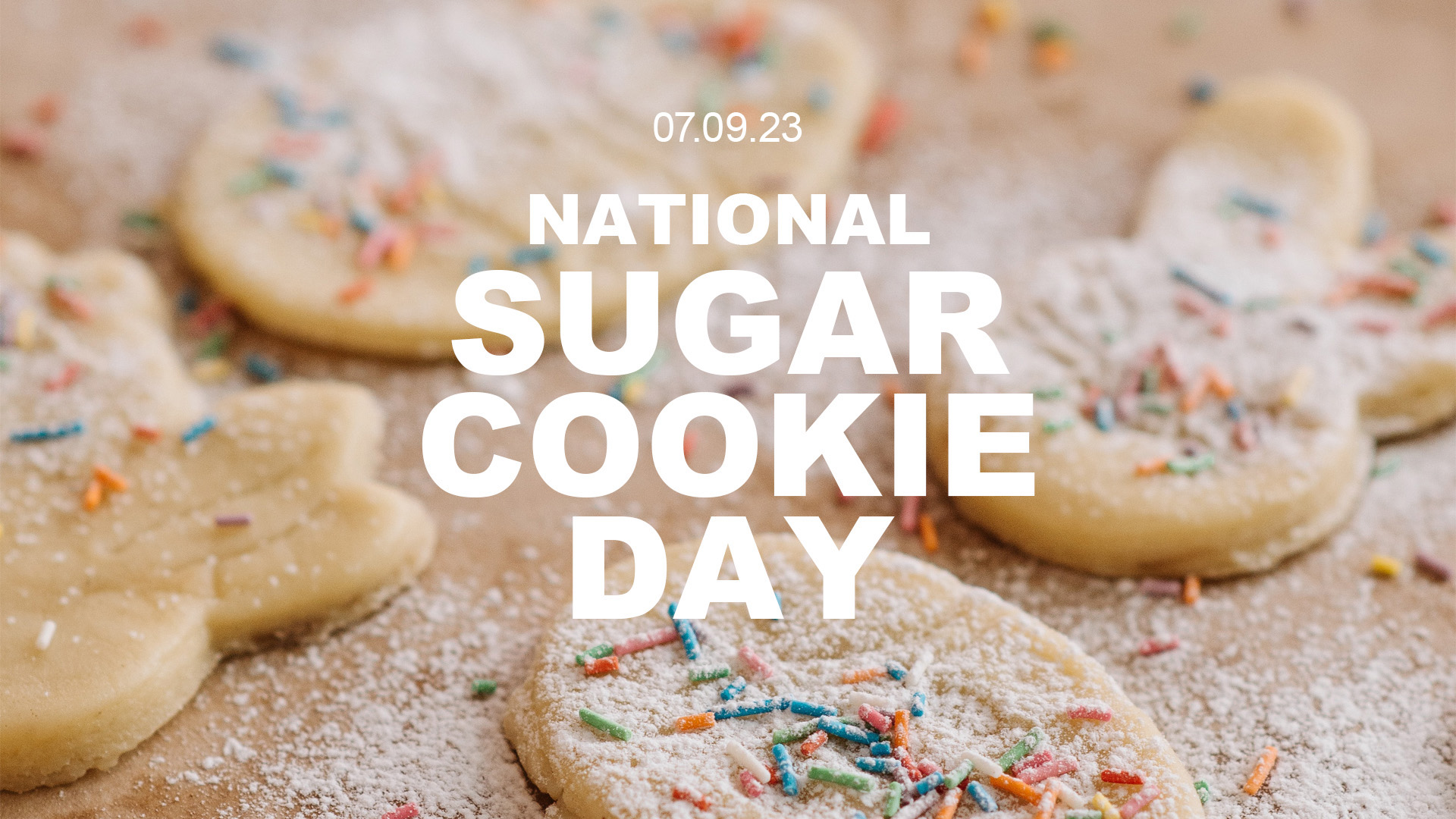 A photo of unbaked sugar cookies laying on tan paper and have a abundant amount of colorful sprinkles. The one cookie that is in the front center of the image is mainly in focus. In the center of the graphic there is white bold font that reads 07.09.23 National Sugar Cookie Day in all caps