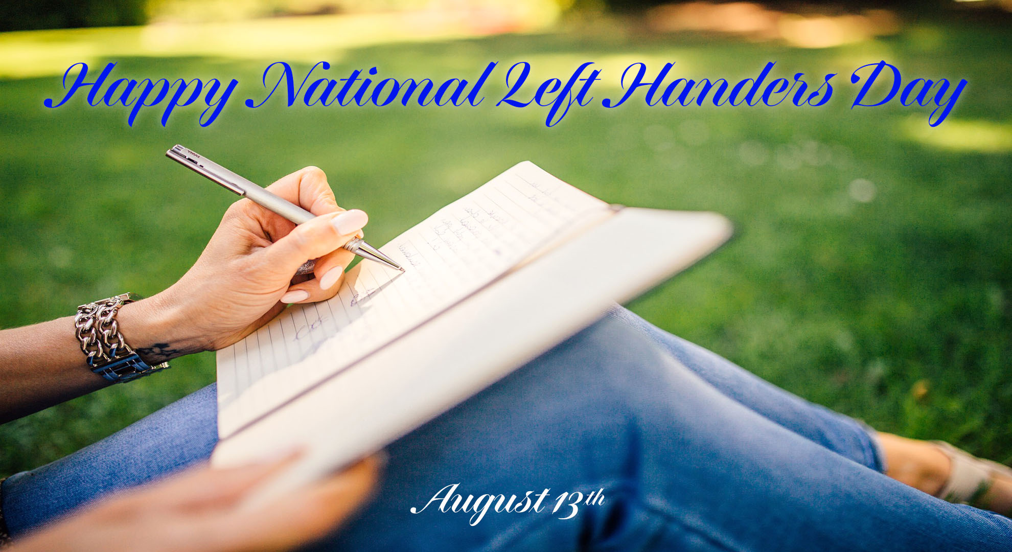 The image is of a person sitting on the ground writing in a journal. They appear to be left handed. Happy NAtional Left Handers Day is written across the top in a vivid blue script font. Towards the bottom middle of the screen August 13th is written in the same white script font.