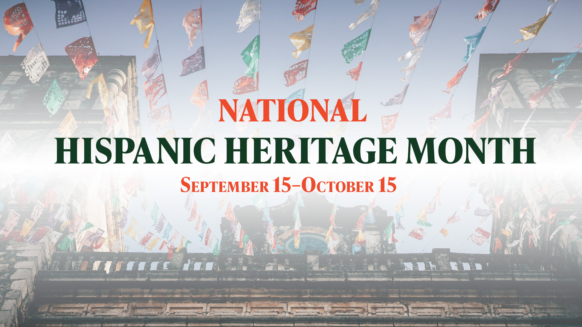 A photo looking up at an old stone building with colorful, rainbow papel picado, paper banner garland hanging off the edge. The center of the image reads National Hispanic Heritage Month September 15–October 15 in red and green serif font letters.