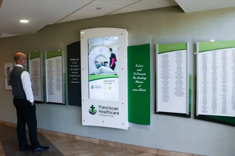 Man standing in front of Arreya's digital and physical donor wall