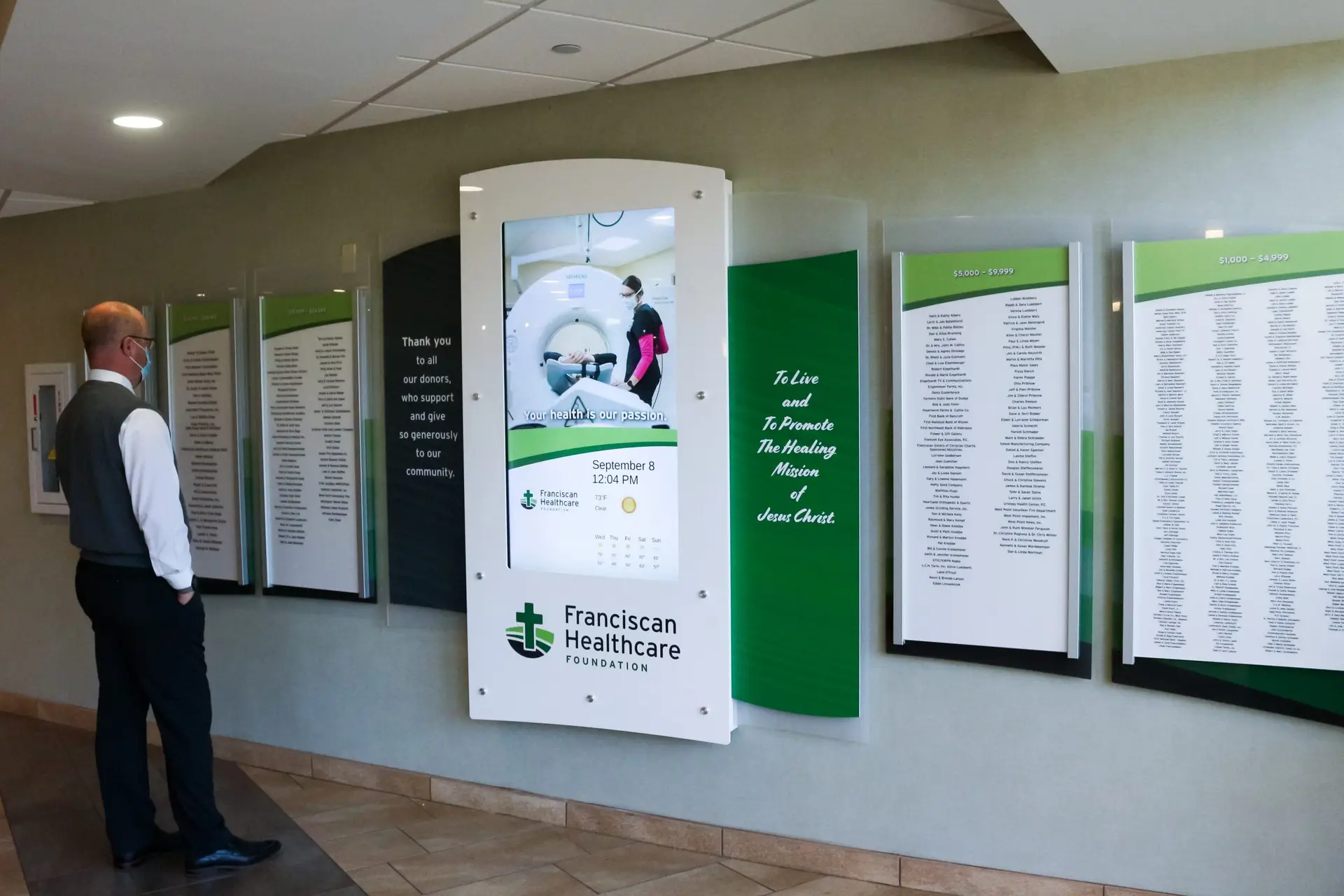 Man standing in front of Arreya's digital and physical donor wall