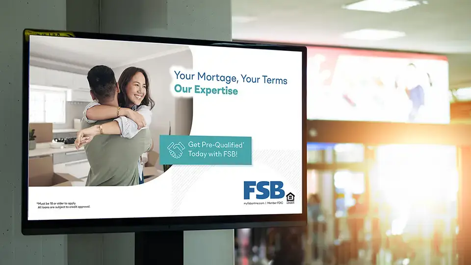 A screen in a bank lobby promotes mortgage rates with an image of a couple hugging in their new home playing on the digital signage slide.