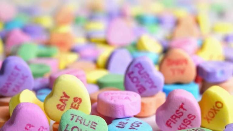 A closeup photo of a multi-colored candy hearts with messages fills the image.