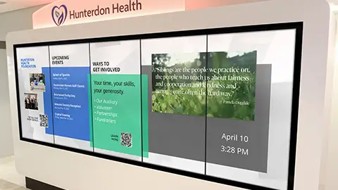 A large white  kiosk with five screens stands in the waiting room of the hospital lobby. Digital Signage content with donor names are scrolling on the screen.