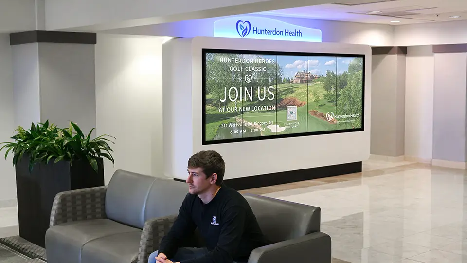 A large white  kiosk with five screens stands in the waiting room of the hospital lobby. Digital Signage content with donor names are scrolling on the screen.