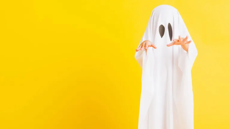 A photo of a kid dressed as a bedsheet ghost, with two drawn on black eyes, sticks their hands straight out. The kid is near the right side and the rest of the graphic is empty. The background is bright yellow.