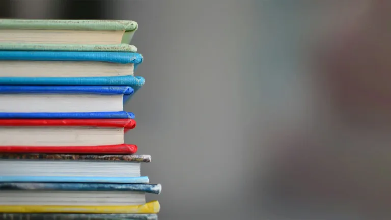 A photo of colorful hard covered books are stacked along the left side. The rest of the photo is blurred out and quite gray in color.