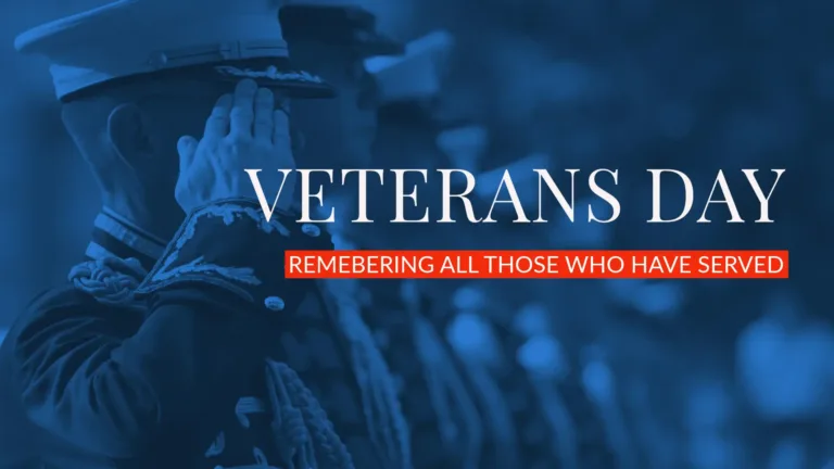 A photo of a line of military men saluting in dress uniforms fade off into the background, while the front most man is in focus near on the left edge. The photo has a duotone filter of black and blue. Right aligned in the center of the graphic is large white words and then a small red horizontal rectangle below it. The large, white serif words read, “VETERANS DAY.” Inside the rectangle, in white, sans letters, reads, "REMEMBERING ALL THOSE WHO HAVE SERVED.”