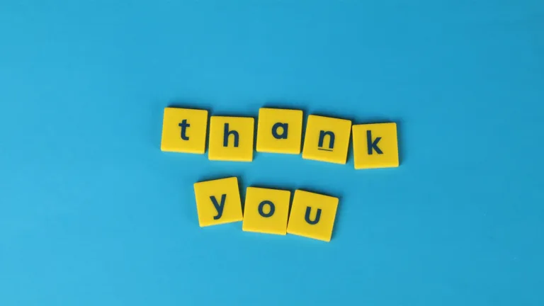 A birds-eye view of yellow plastic squares on top of a solid blue surface. The squares are in the center of the photo and spell out thank you. The letters in the squares each use the same navy, lower case, bold sans font.