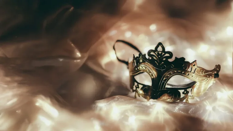 An ai generated photo of a gold party eye mask laying on shimmery off white fabric. The fabric fades into a dark background.