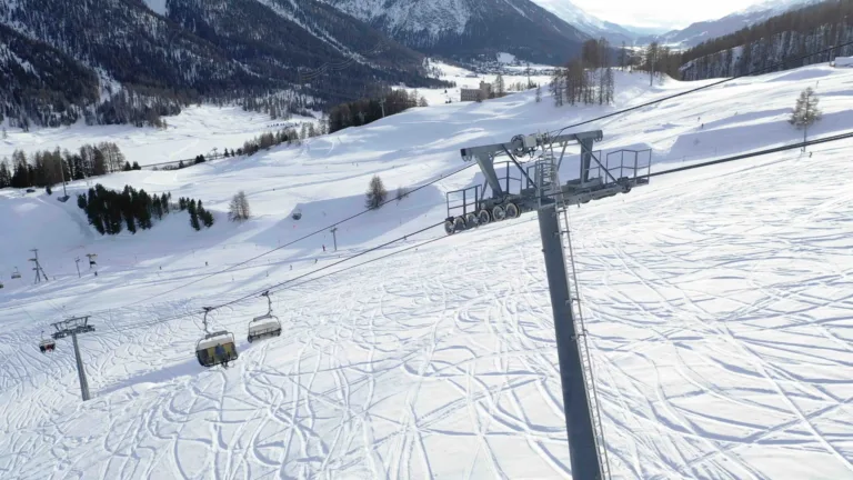 A video of a ski lift moving with no people on it. The lift in a mountain range. The snow underneath it is covered in ski tracks.