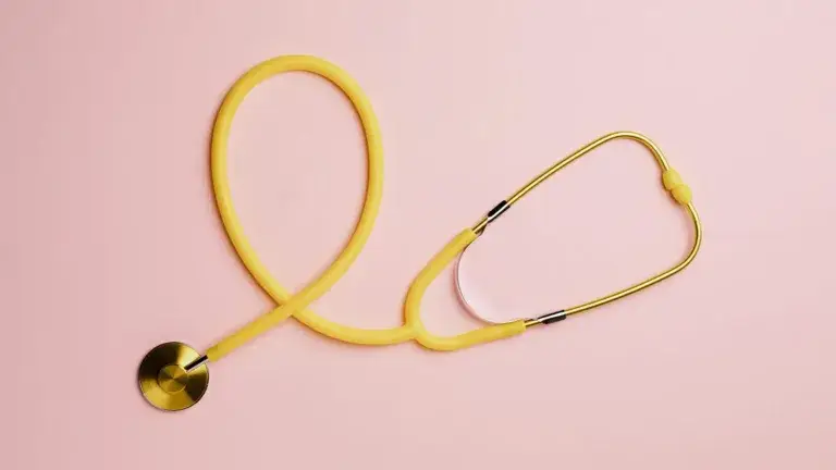 A birds-eye view of a yellow stethoscope on top of a light pink background.