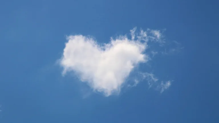 A photo of a fluffy white, heart shaped cloud against a clear blue sky.