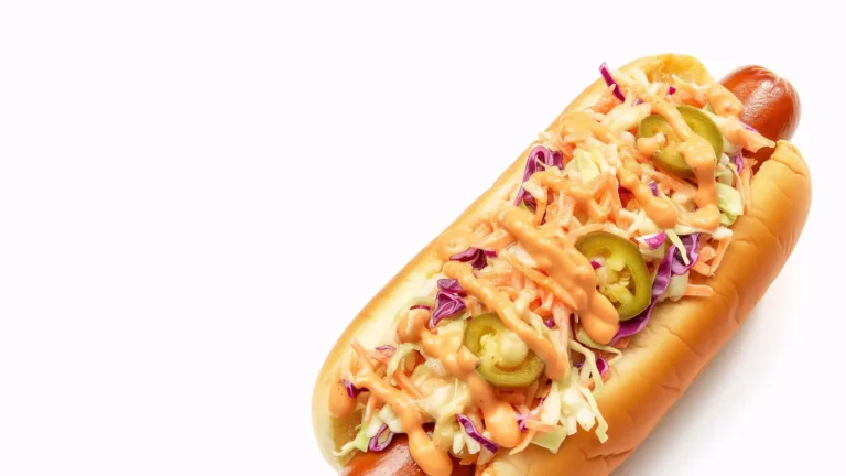 A photo of a hot dog in a bun fills the center to top right corner of the graphic. The background is solid white. The hot dog is covered in toppings, such as slaw, jalapenos, and an orange sauce.