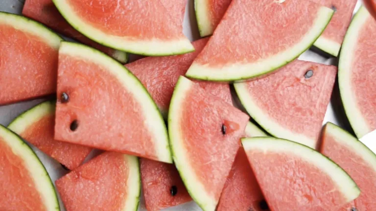 Triangle slices of watermelon are laid out on a stainless steel counter. A person's hands are come in and lay more slices of watermelon down—filling the entire video image and counter surface.